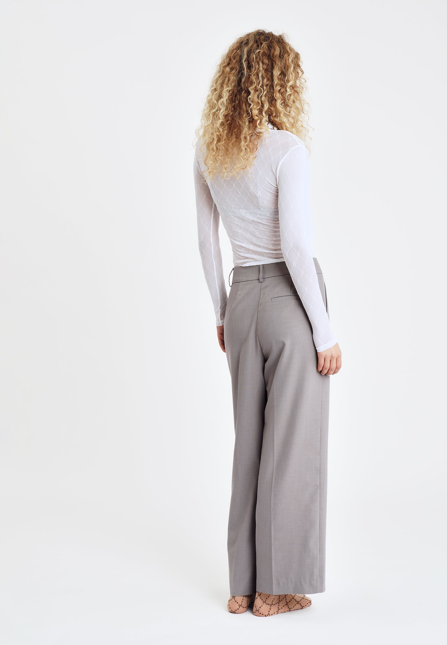 En person med krøllet hår har en HYPE THE DETAIL Mesh-bluse i offwhite på og står med ryggen til kameraet.