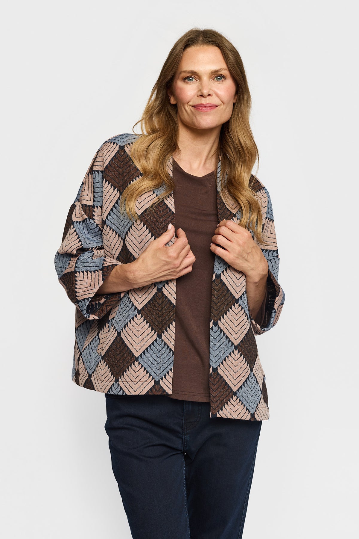 En kvinde har en brun T-shirt, mørke jeans og en 156303 | 2-Biz - Danielle Brun-jakke med diamantmønster på.