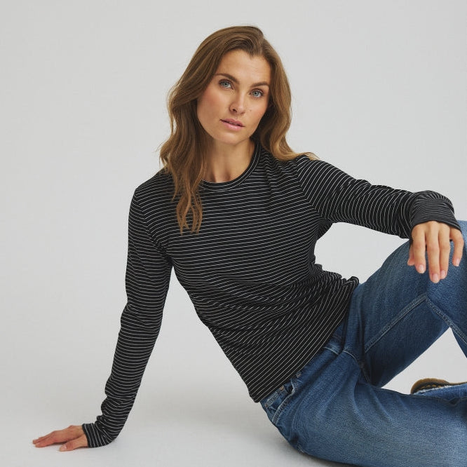 En kvinde iført en 156423 | Luxzuz - Segberg Sort sort langærmet T-shirt med tynde hvide striber og blå jeans.