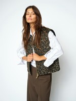 En kvinde har en MOS MOSH Elise Leopard-vest på sammen med en hvid bluse og brune bukser og står foran en ensfarvet lys baggrund.
