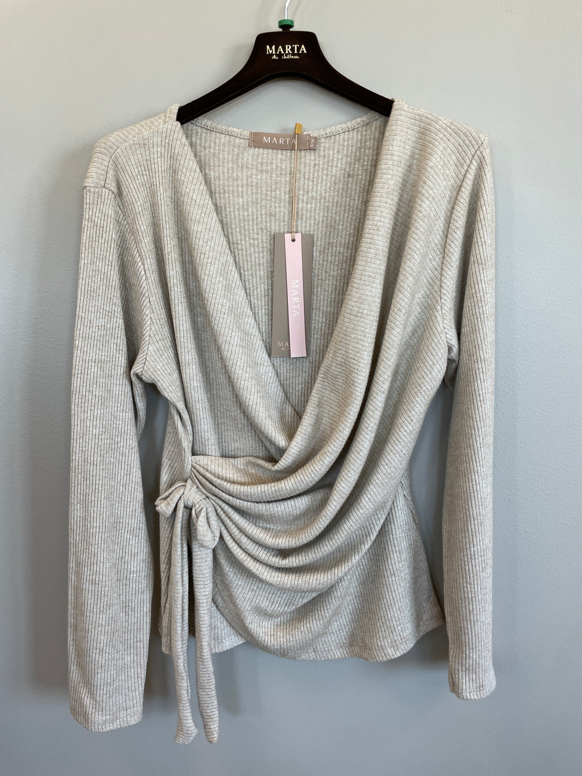 Marta du Château MDCTalina Beige ribbet langærmet wrap-top med bindebånd i siden, vist på en bøjle foran en ensfarvet væg.