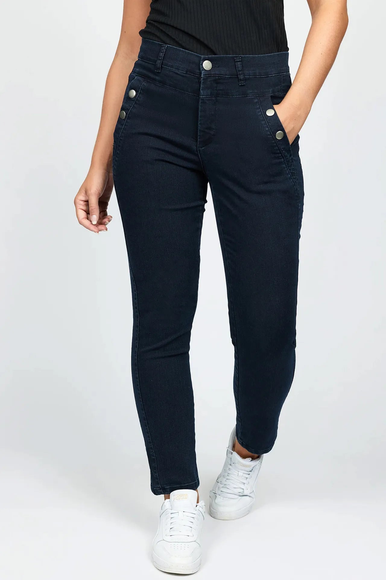 En person iført 2-Biz Karcemona mørkeblå jeans, sort top, hvide sneakers, med den ene hånd i lommen.