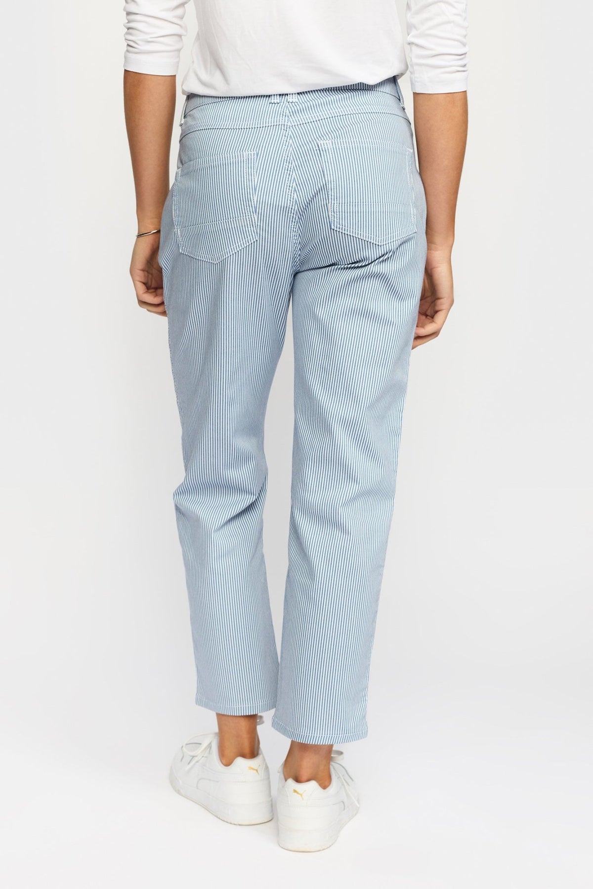 En person iført 2-Biz Bay Blå bukser, hvide sneakers og en hvid bluse, set bagfra.