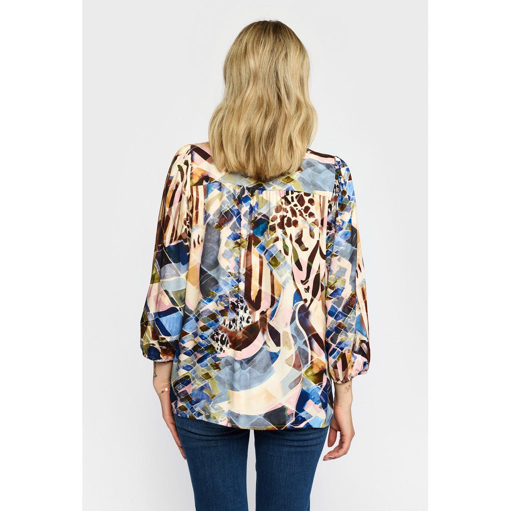 Kvinde med skulderlangt blondt hår iført en mønstret bluse fra 2-Biz Laura Blå og blå jeans, set bagfra.