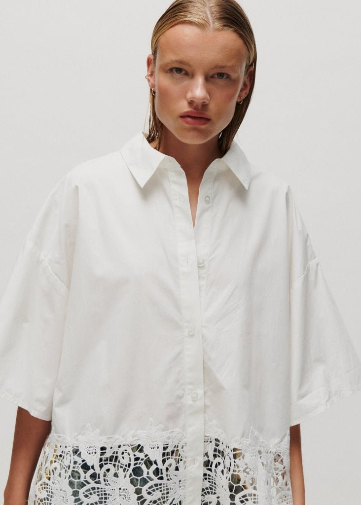 Modellen bærer en 2NDDAY Edith-skjorte i offwhite 155112 med hæklet blonderkant og poserer foran en ensfarvet baggrund.