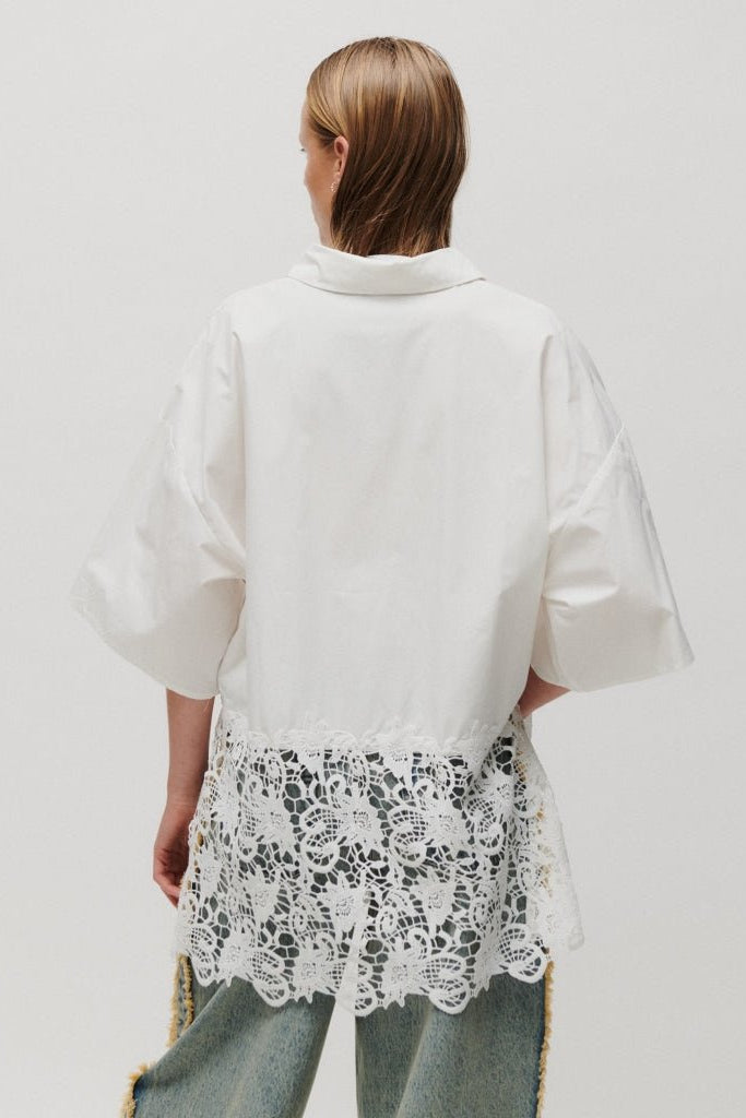 Person, der står med ryggen til, iført en 2NDDAY Edith-skjorte i offwhite med lyse kanter, blå jeans og en ensfarvet baggrund.