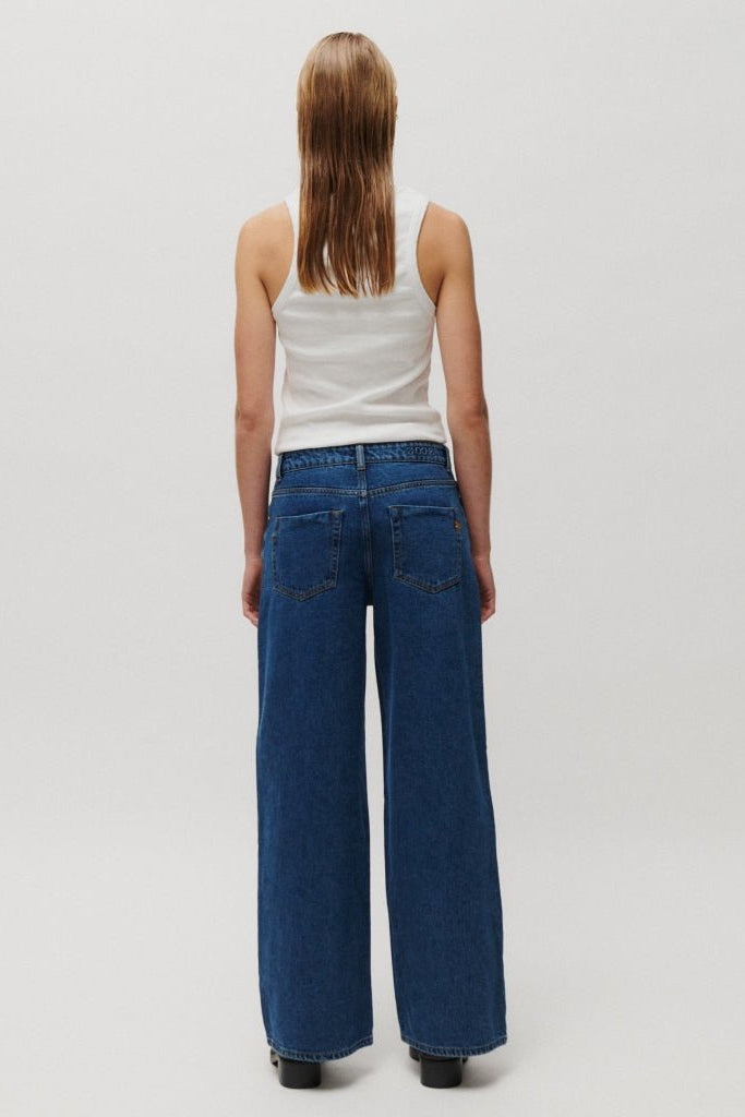 En person med vådt hår har en hvid tanktop og 2NDDAY Roden Denim-jeans i mellemblå på og står med ryggen til.