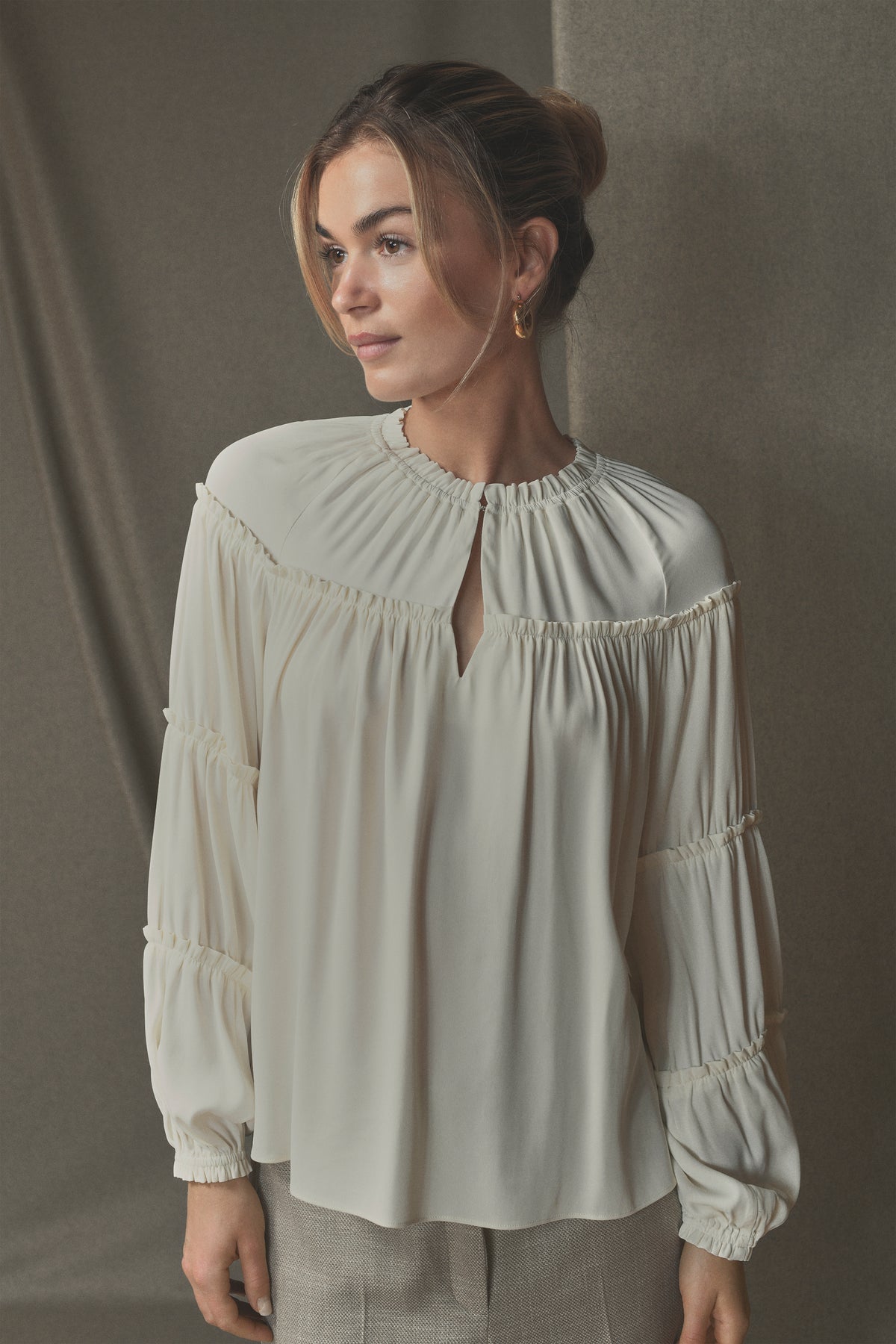 En kvinde iført Gustavs Annsofie-bluse i offwhite med rynkede detaljer og ballonærmer foran en neutral baggrund.
