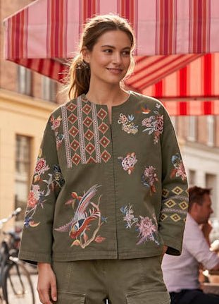 Kvinde udendørs i en Amaze Cph Noa Army grøn jakke med farverige blomster- og geometriske broderidetaljer.