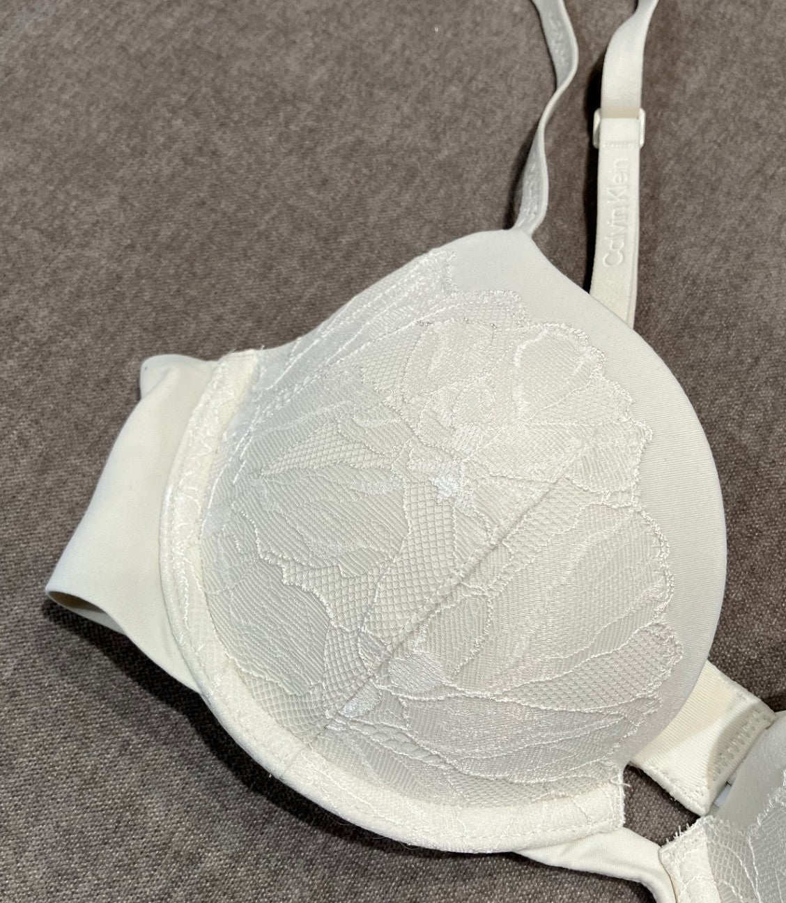 Calvin Klein YAE beige blonder-bh med blomstermønster på en grå stofbaggrund.