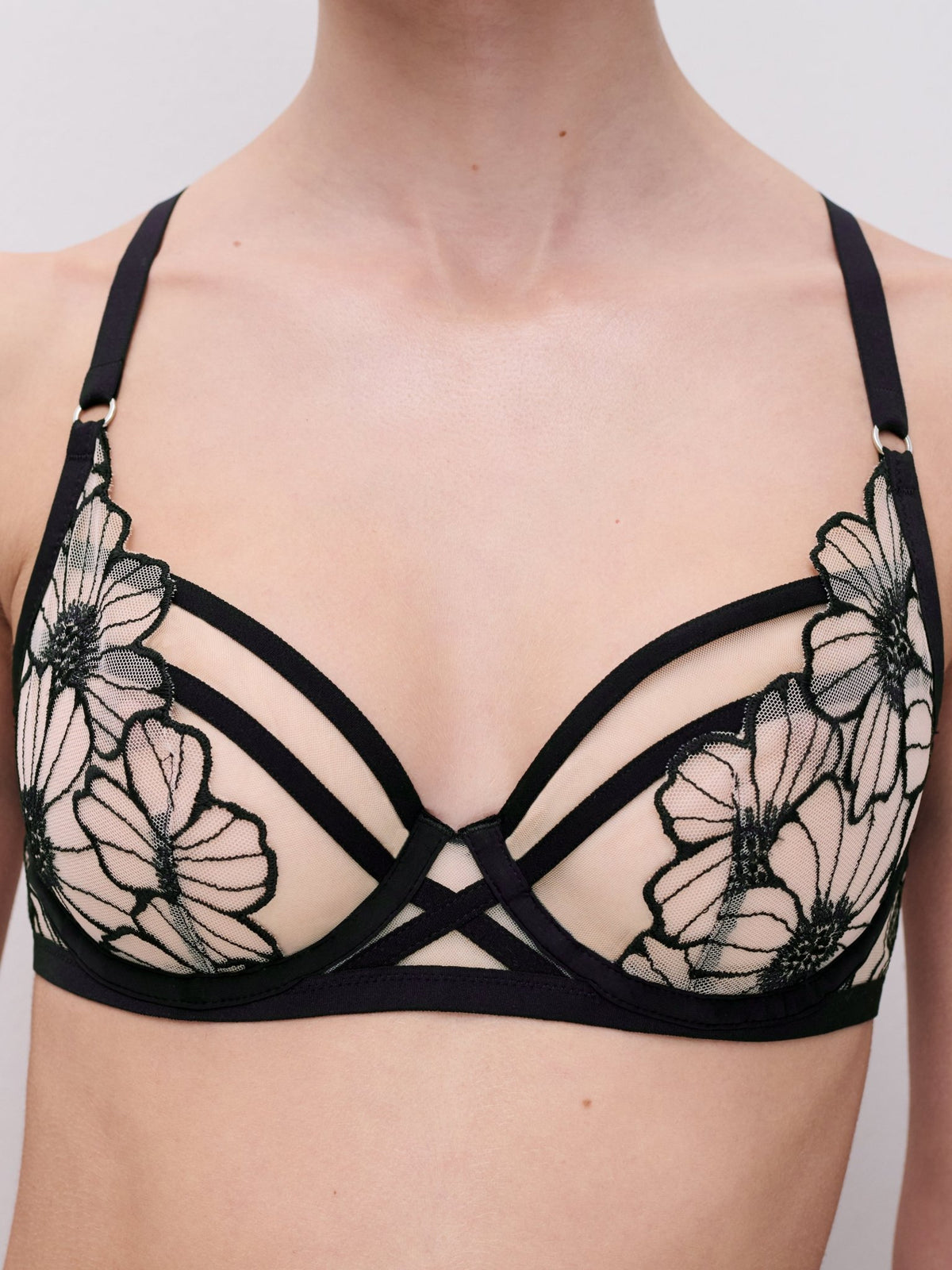 Model iført en Chantelle Lush-bh i sort/blød rosa med net og blomsterdetaljer, fotograferet på en ensfarvet baggrund.