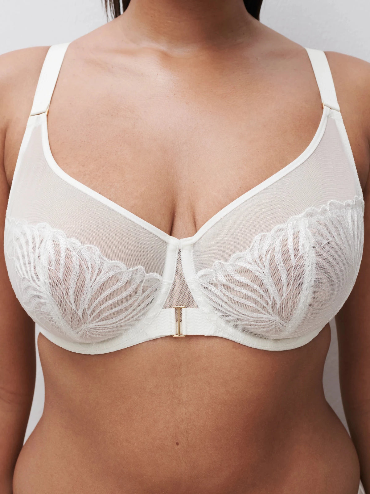 Modellen på billedet, der viser midten af overkroppen, bærer Chantelle Legend Milk Off white, en gennemsigtig blonder-bh med bladbroderi og bøjle.