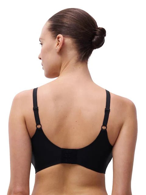 En kvinde med håret sat op i en knold bærer en Chantelle Seamless 152392 Soft Stretch Power Sort-bh, set bagfra på hvid baggrund.