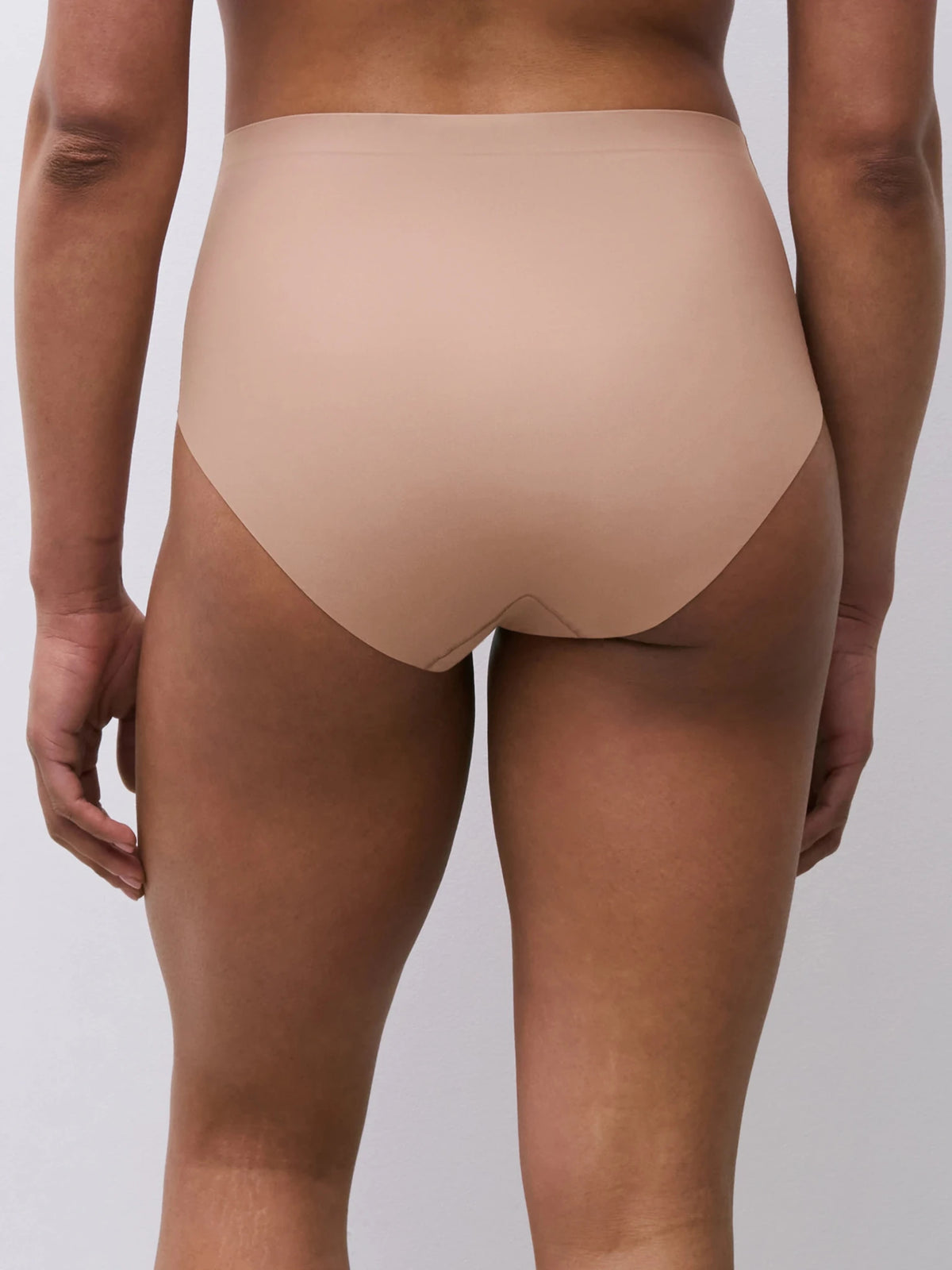 Modellen bærer Chantelle Seamless – Defi Latté 155789, nudefarvet undertøj med høj talje, vist bagfra på en ensfarvet baggrund.