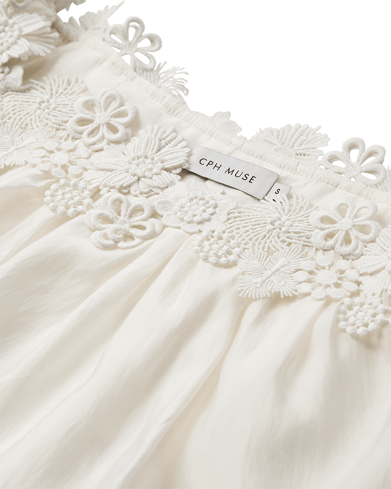 Nærbillede af Copenhagen Muse Molly-top i offwhite med blomsterblonder og CPH MUSE S-mærke.