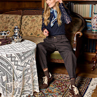 En kvinde sidder på en vintage-sofa iført bukser fra Black Colour – modellen »Mille Kaffe«.