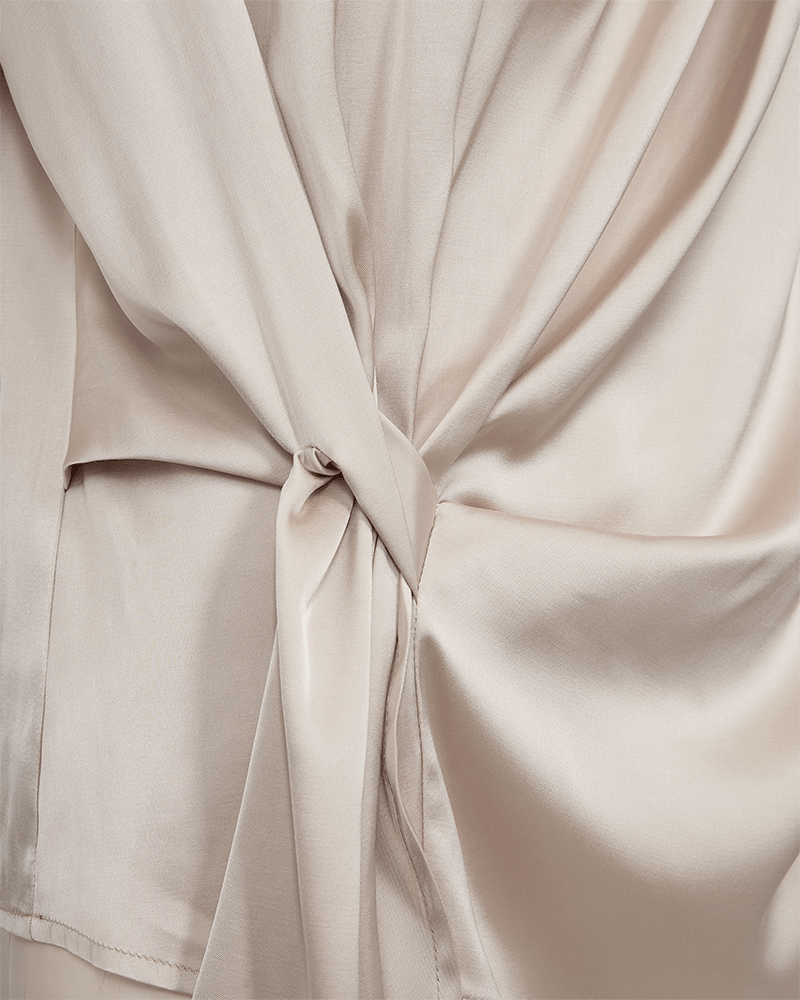 Nærbillede af Freequent – Dova Beige satinbluse med knudedetalje og blødt, asymmetrisk fald.