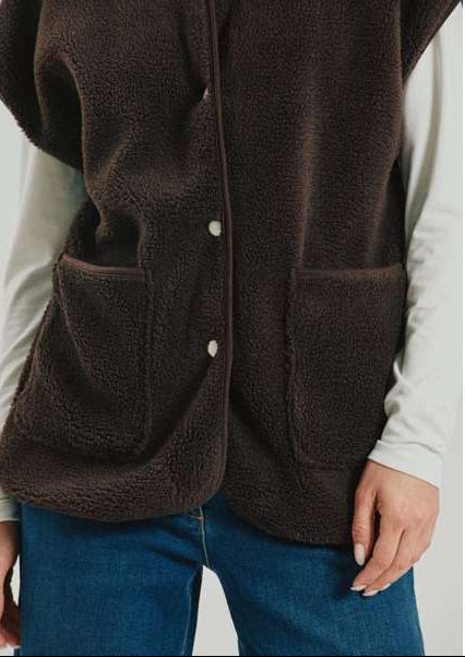 Personen har en Freequent 155609 Teddy Mørkebrun vest med lommer på over en langærmet skjorte og blå jeans.