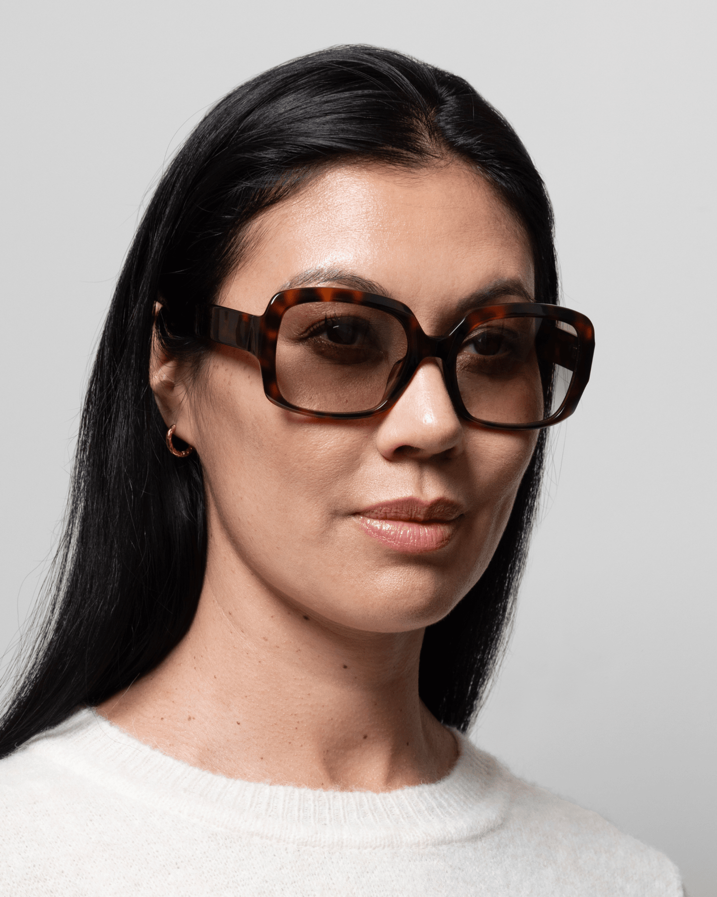 Kvinde med glat, sort hår i GLAS – med briller med Isabella Brun-mønster og en hvid sweater, der vender let mod højre.