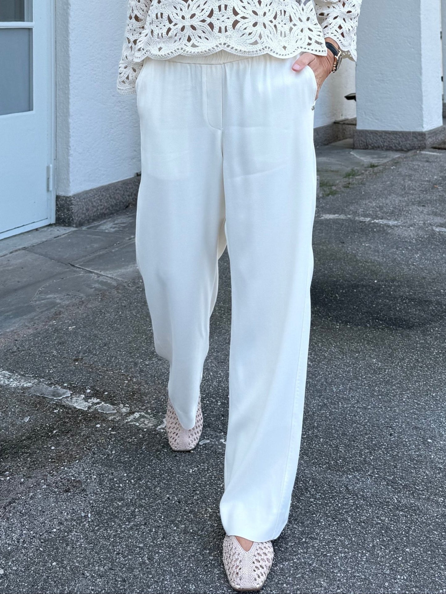 En person har Gustavs »Bali Off White«-bukser, en hæklet top og vævede sko på sig på en brolagt udendørsflade.