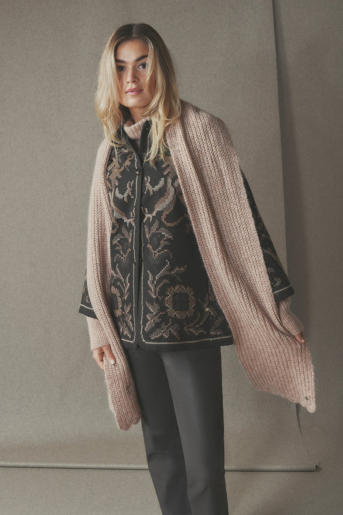 Kvinde iført en sort mønstret 156402 | Gustav - Sarah Sort mønstret blazer under et bredt beige tørklæde og mørke bukser.