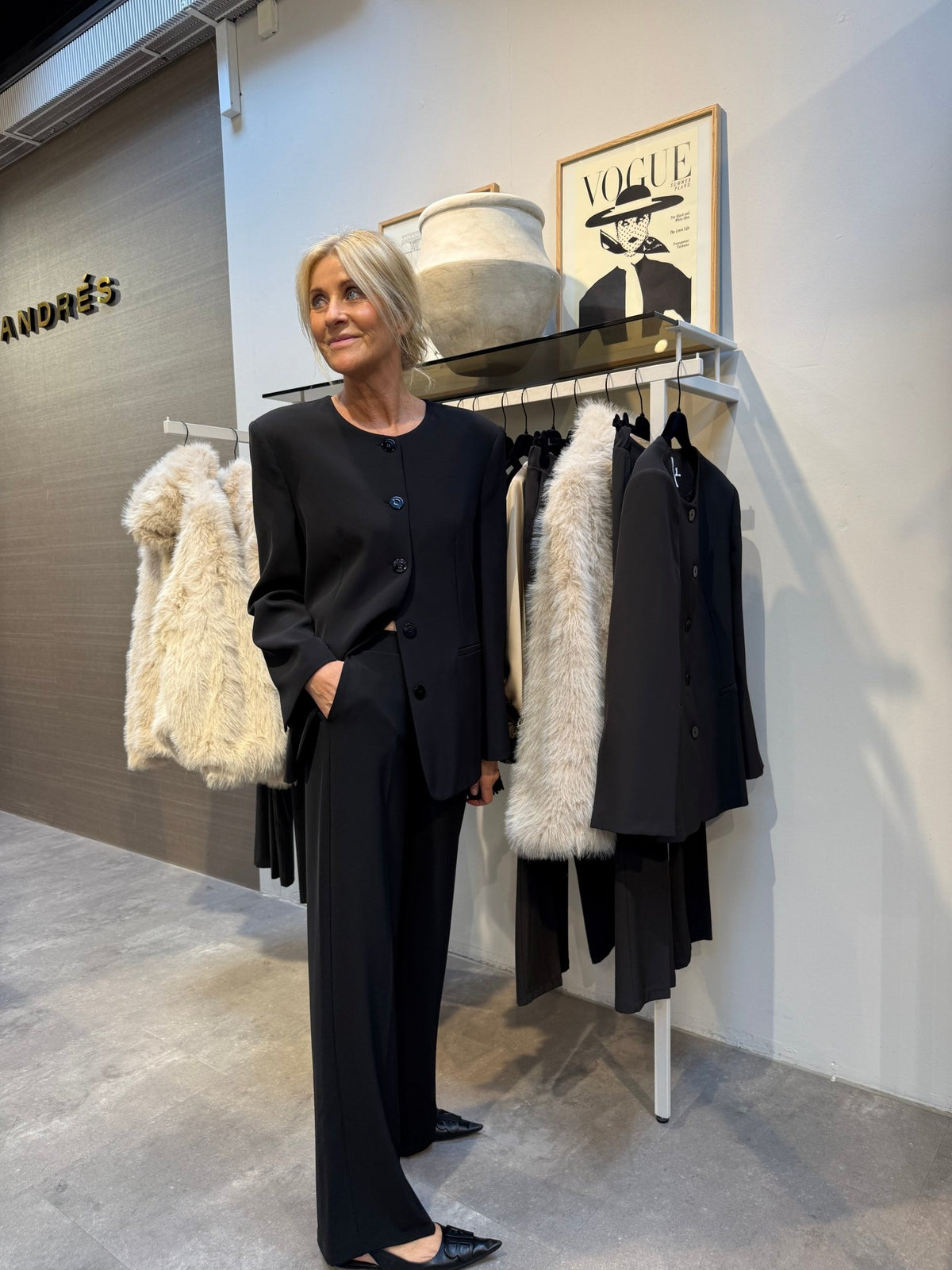 En kvinde har en Imperial 155964 JCA9 Sort-blazer på i en butik med frakker og kunstværker med Vogue-tema på væggene.