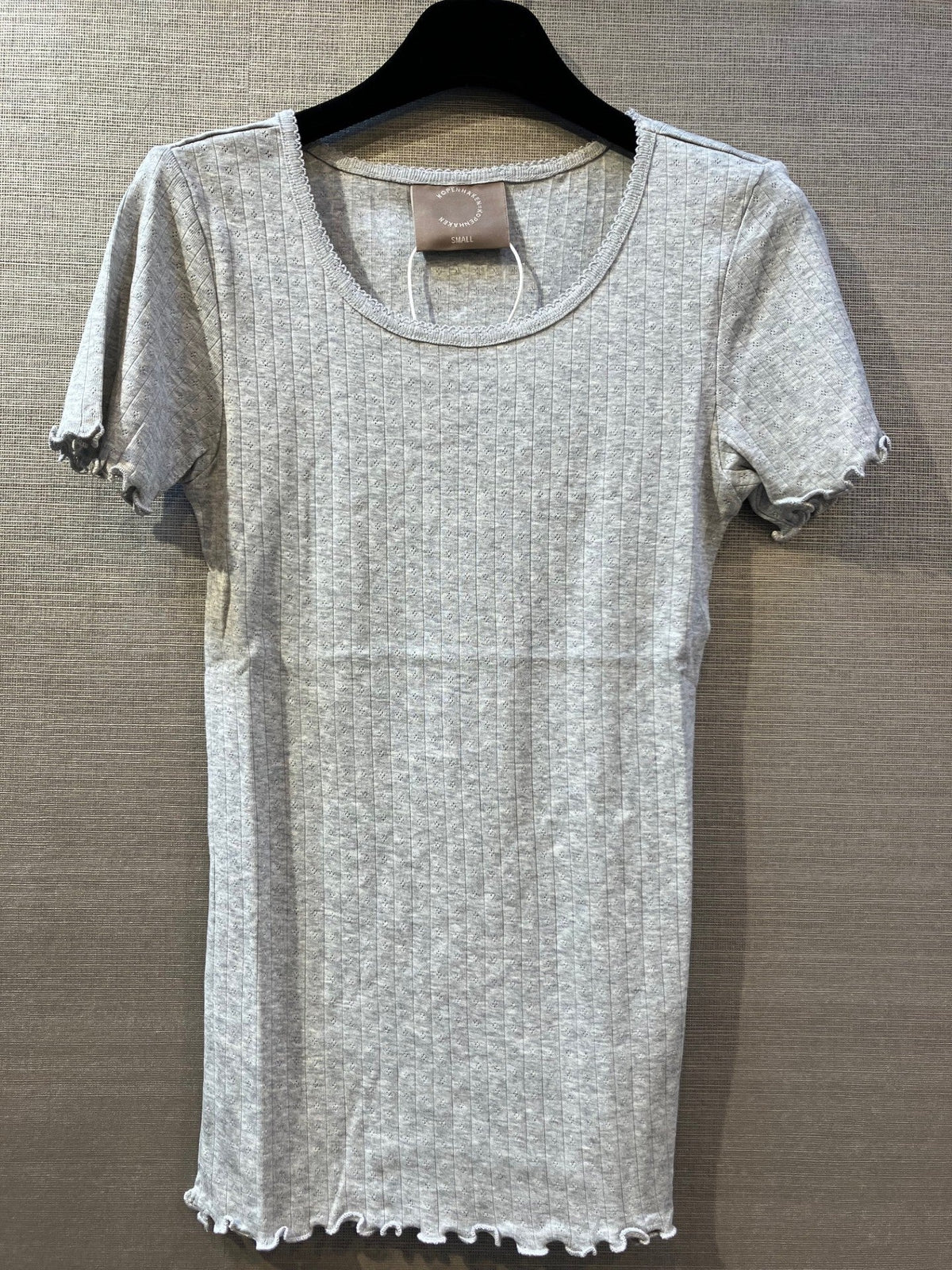 Kopenhaken Soft Tee Grå 154491 i lysegrå bomuld med bølgekant, på sort bøjle og beige baggrund.