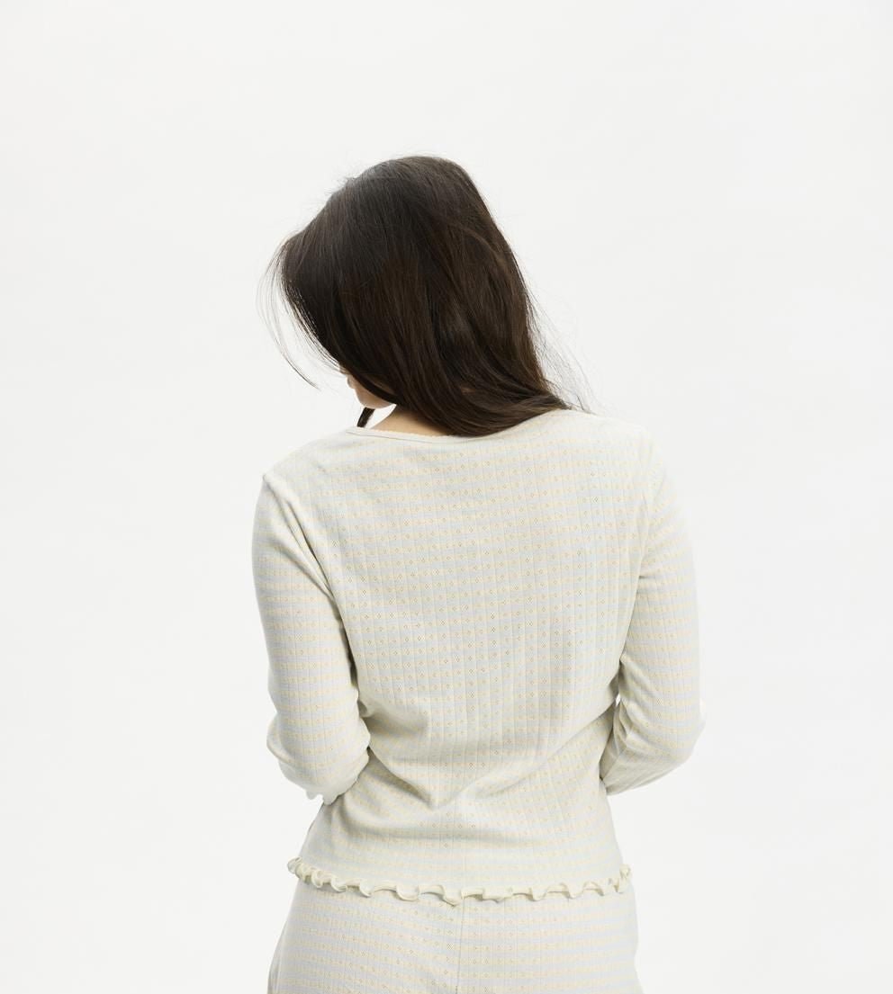 En person med langt hår har en lyseblå Kopenhaken Soft Stripe-cardigan på og står med ryggen til foran en hvid baggrund.