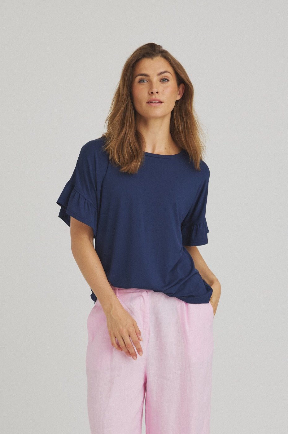 Modellen bærer en Luxzuz 155099 Sejla mørkeblå T-shirt med flæser og lyserøde bukser foran en ensfarvet baggrund.