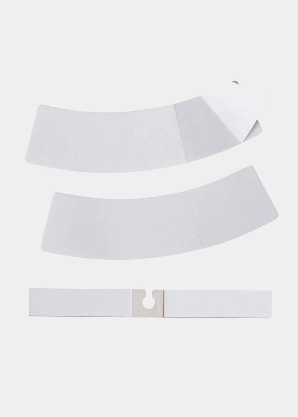 Tre hvide strimler af Magic Bodyfashion Dress Tape, hvoraf den ene er delvist afdækket, vist på en ensfarvet hvid baggrund.