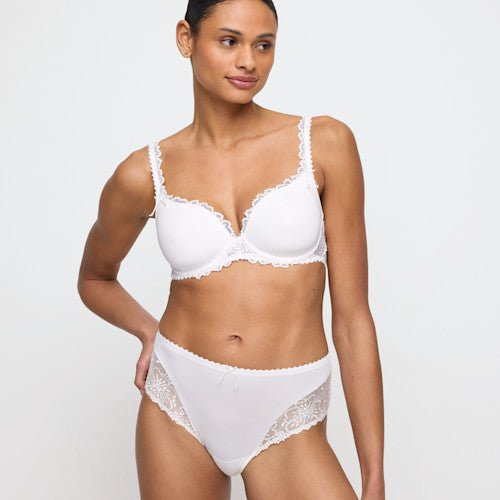 En kvinde iført en Marie Jo - Jane Natural Off-white 130001-bh og maxitrusse står foran en ensfarvet baggrund og kigger mod venstre.