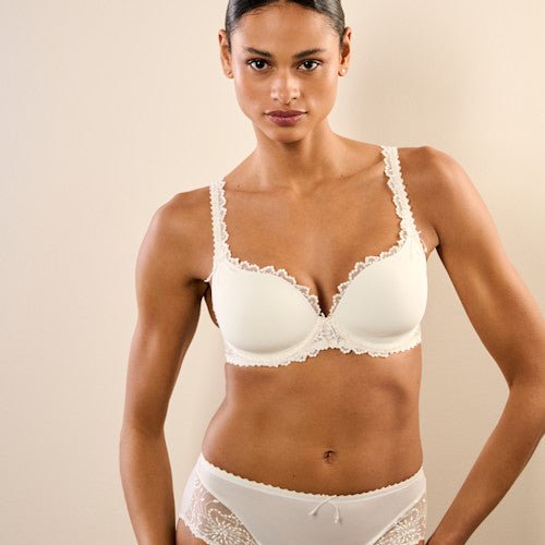 Kvinde iført en Marie Jo Jane Natural off-white-bh og maxitrusse, stående foran en lys baggrund.