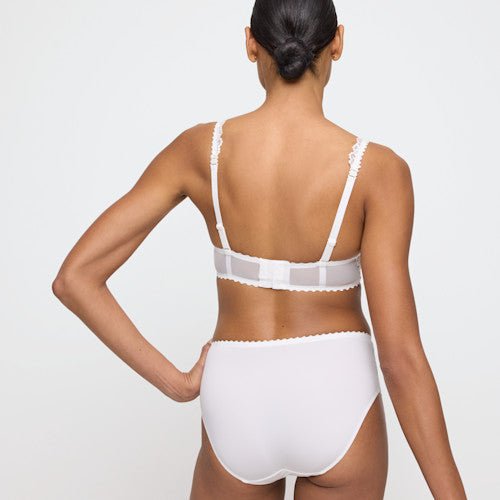 En person står med ryggen til kameraet iført en Marie Jo Jane Natural Off-white-bh og maxitrusse på en ensfarvet lys baggrund.