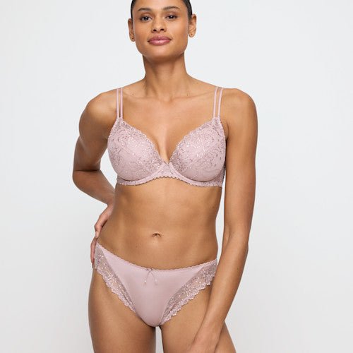 En kvinde står med ansigtet vendt fremad iført en Marie Jo - Jane Bois De Rose Rosa 144410-bh, lyserød med blonder, foran en ensfarvet baggrund.