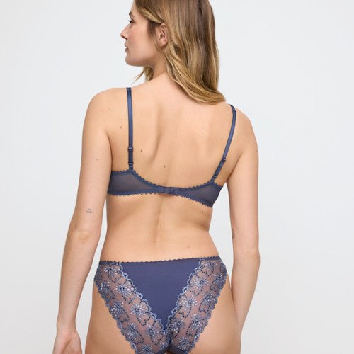 Kvinde, der står med ryggen til, iført et Marie Jo - Jane Blue Shadow Blå-blonder-sæt med push-up-bh, foran en neutral baggrund.