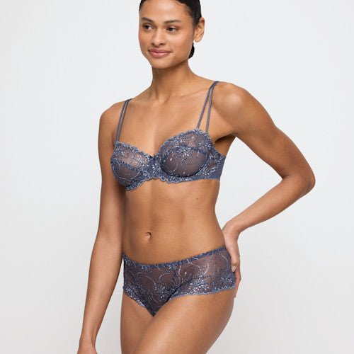 Modellen bærer en Marie Jo Jane Blue Shadow Blå balconette-bh i blonder og hipster-trusser på en grå baggrund.