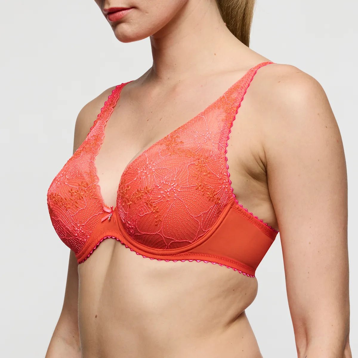 Modellen bærer en Marie Jo - Solene Orange 154359-bh med blomsterbroderi, vist fra siden på en ensfarvet baggrund.