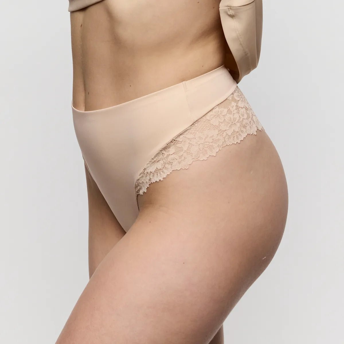 En model iført Marie Jo 154738 Soft Studio Caffe Latte Pudder – beige undertøj med høj talje og blondedetaljer fra taljen ned til låret.