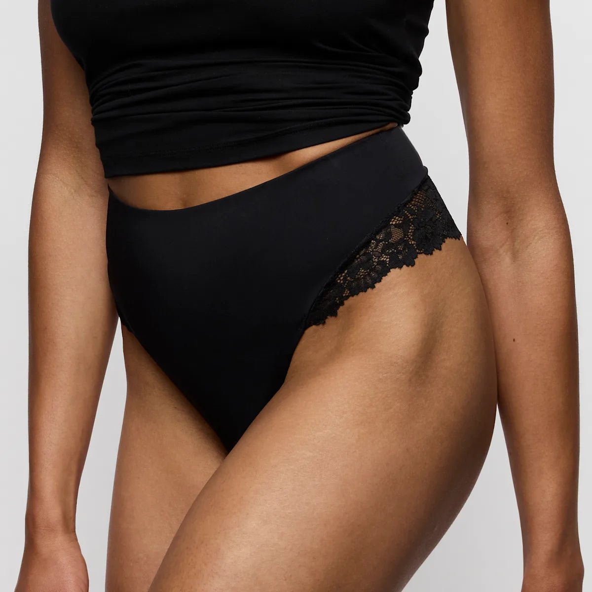Kvinde iført en sort G-streng med høj talje fra Marie Jo Soft Studio og en sort crop top, vist fra midten af overkroppen til låret.