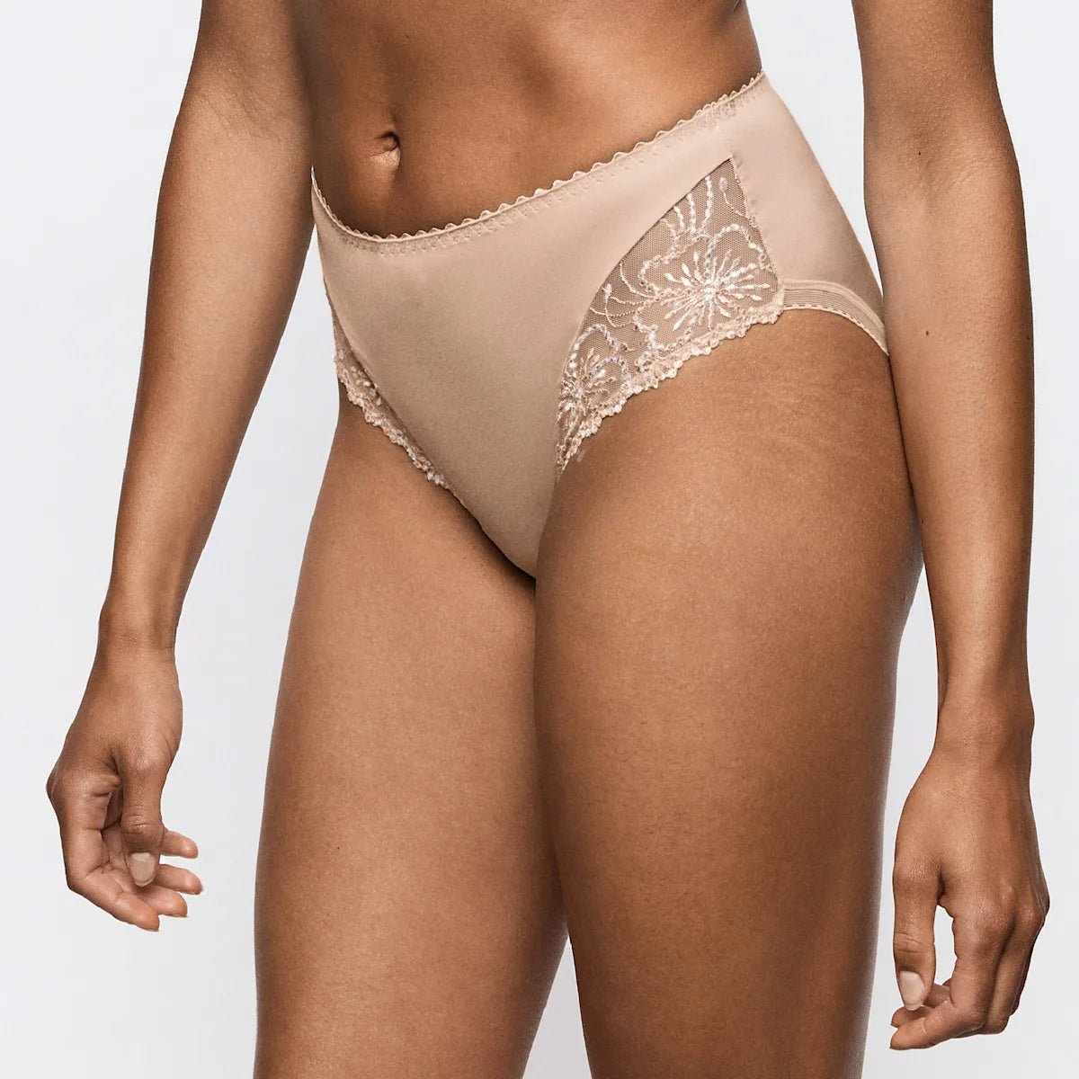 En model har Marie Jo 155100 Jane Sand Sand-trusser med høj talje på; her ses modellen med blonder og trusserne, der går fra taljen til midt på låret.