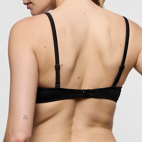 Bagfra-billede af en person iført en Marie Jo Swim - Cassie Black Sort bikini-top, hvor der ses en lille tatovering tæt på venstre albue.