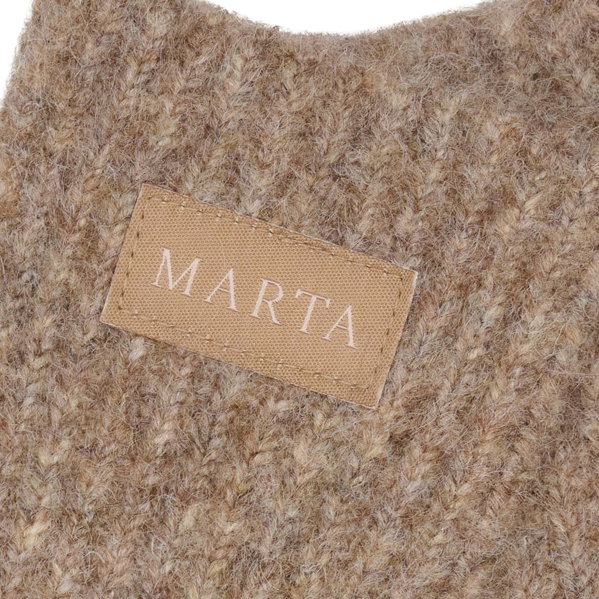 Beige stofmærke med påskriften »MARTA« på 152749 Vanessa Lysebrun fra Marta du Château, syet fast på et lysebrunt strikket håndklæde.