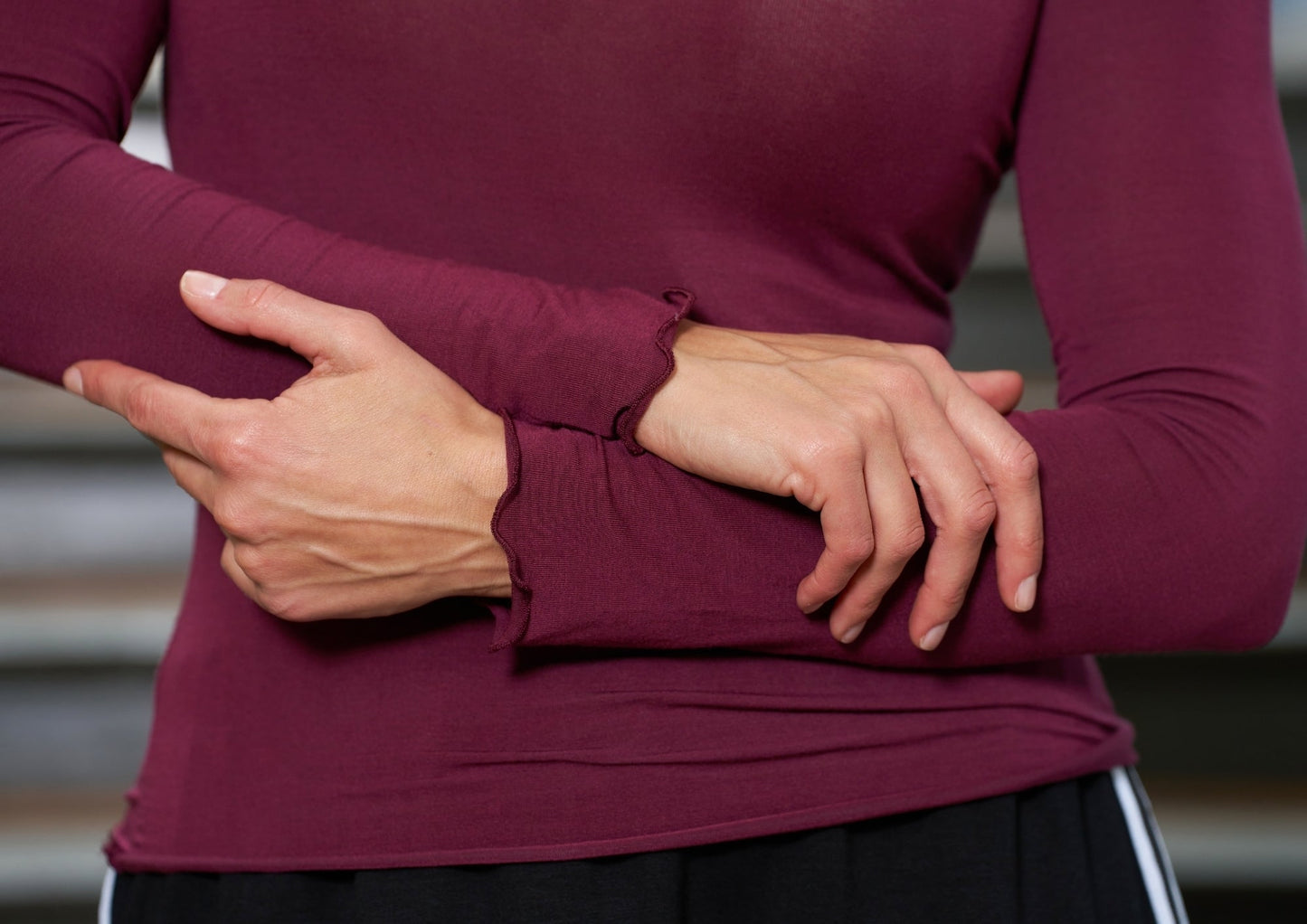 Personen, der har Marta du Château’s Leonora Bordeaux-top på, holder sin venstre underarm med højre hånd, mens vedkommende står indendørs.