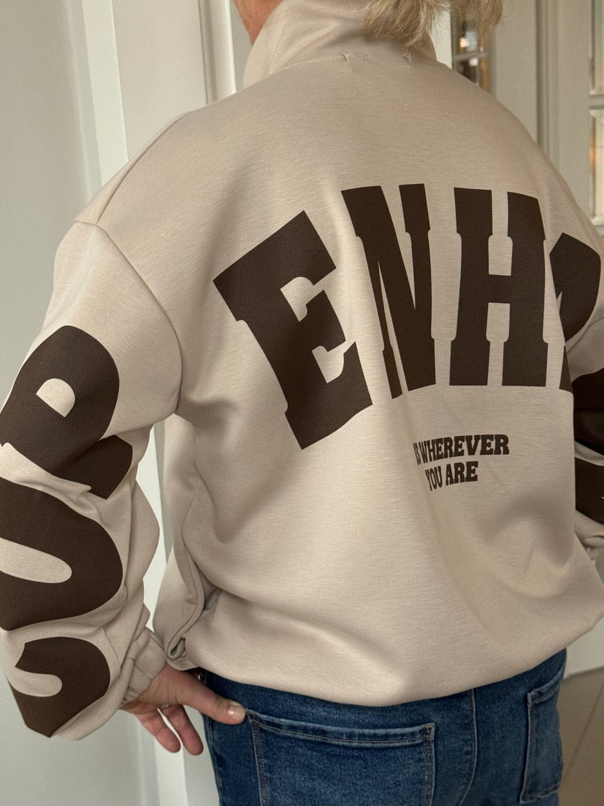 Personen har en beige Marta du Château Nete-sweatshirt på med teksten »ENH« og »WHEREVER YOU ARE« på ryggen.