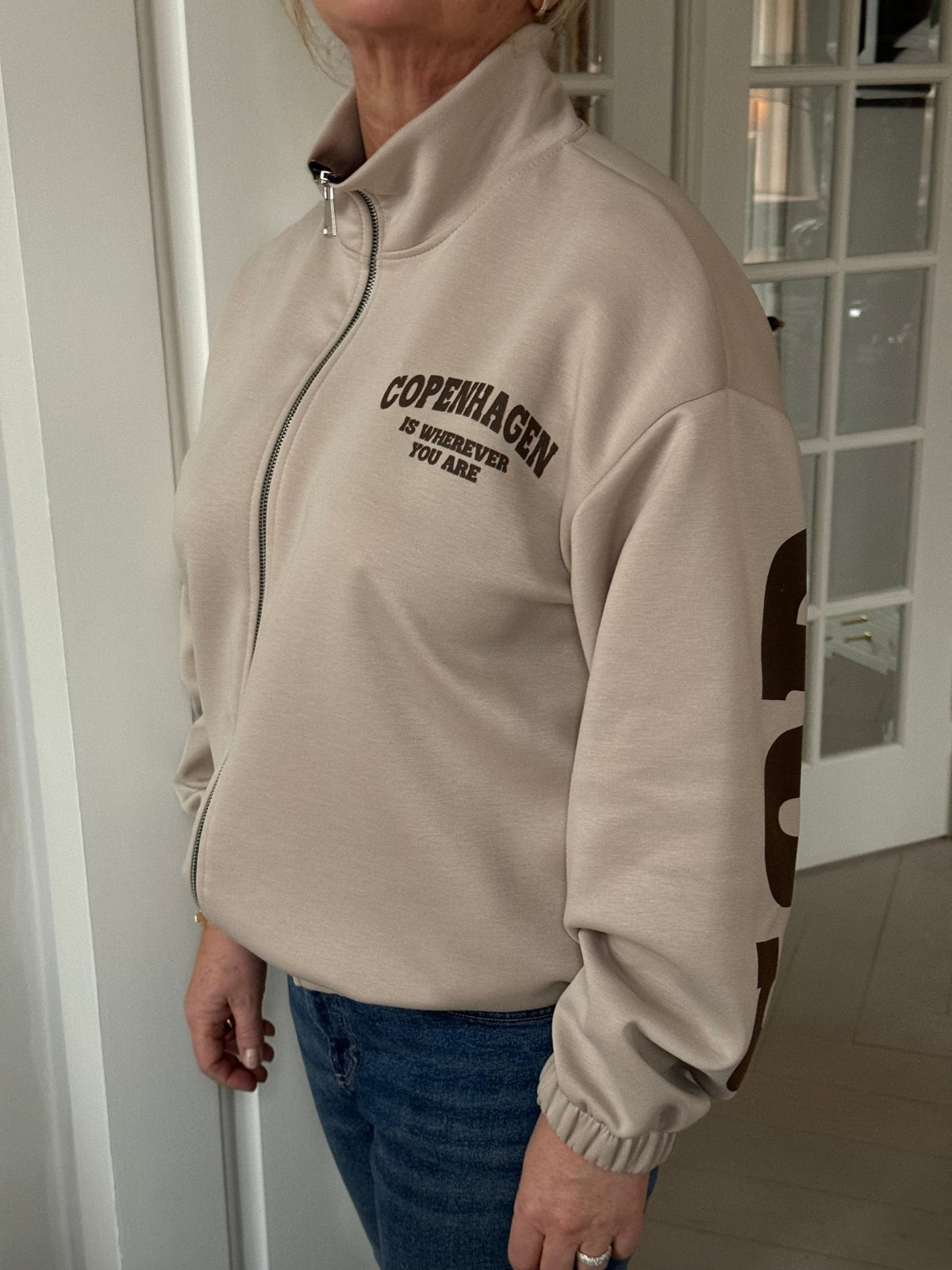 En person, der har Marta du Château’s Nete Beige-sweatshirt på med teksten »Copenhagen is wherever you are«, står ved en dør.