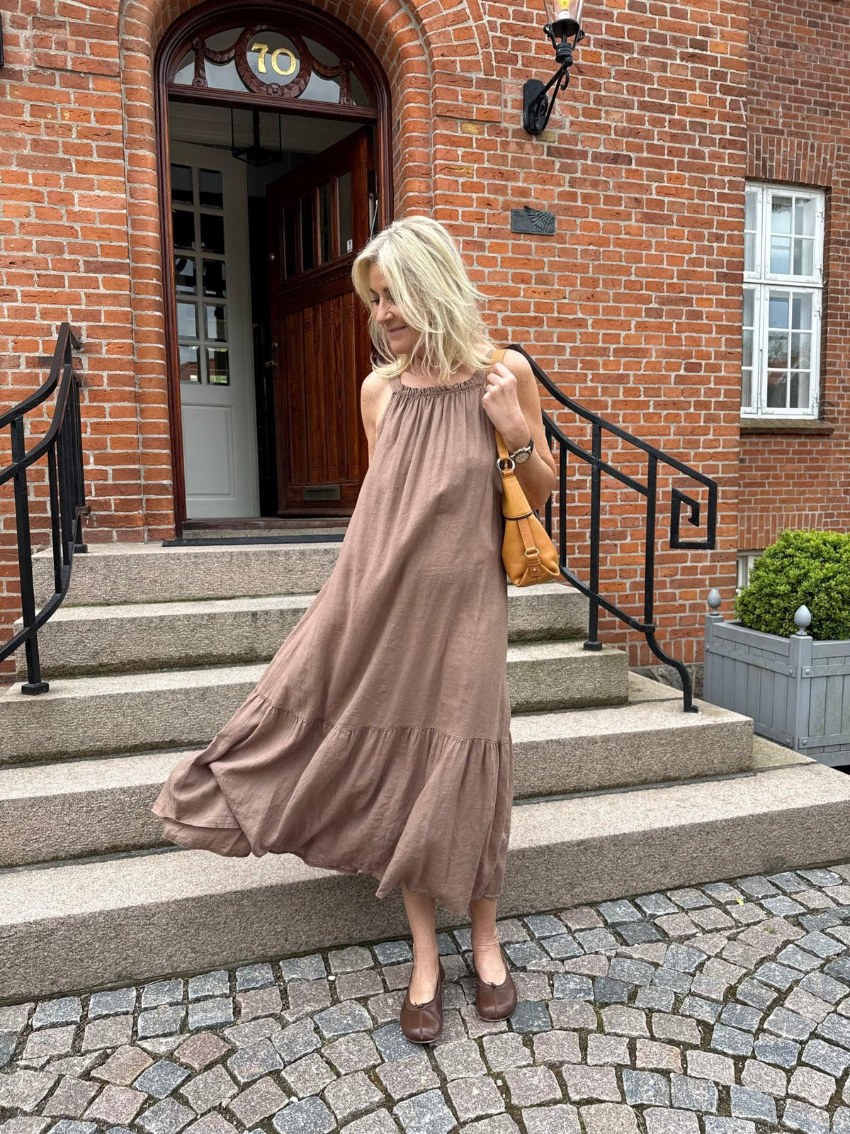 En kvinde iført en kjole fra Marta du Château Valisse Brun står på en stentrappe og udstråler en naturlig stil.