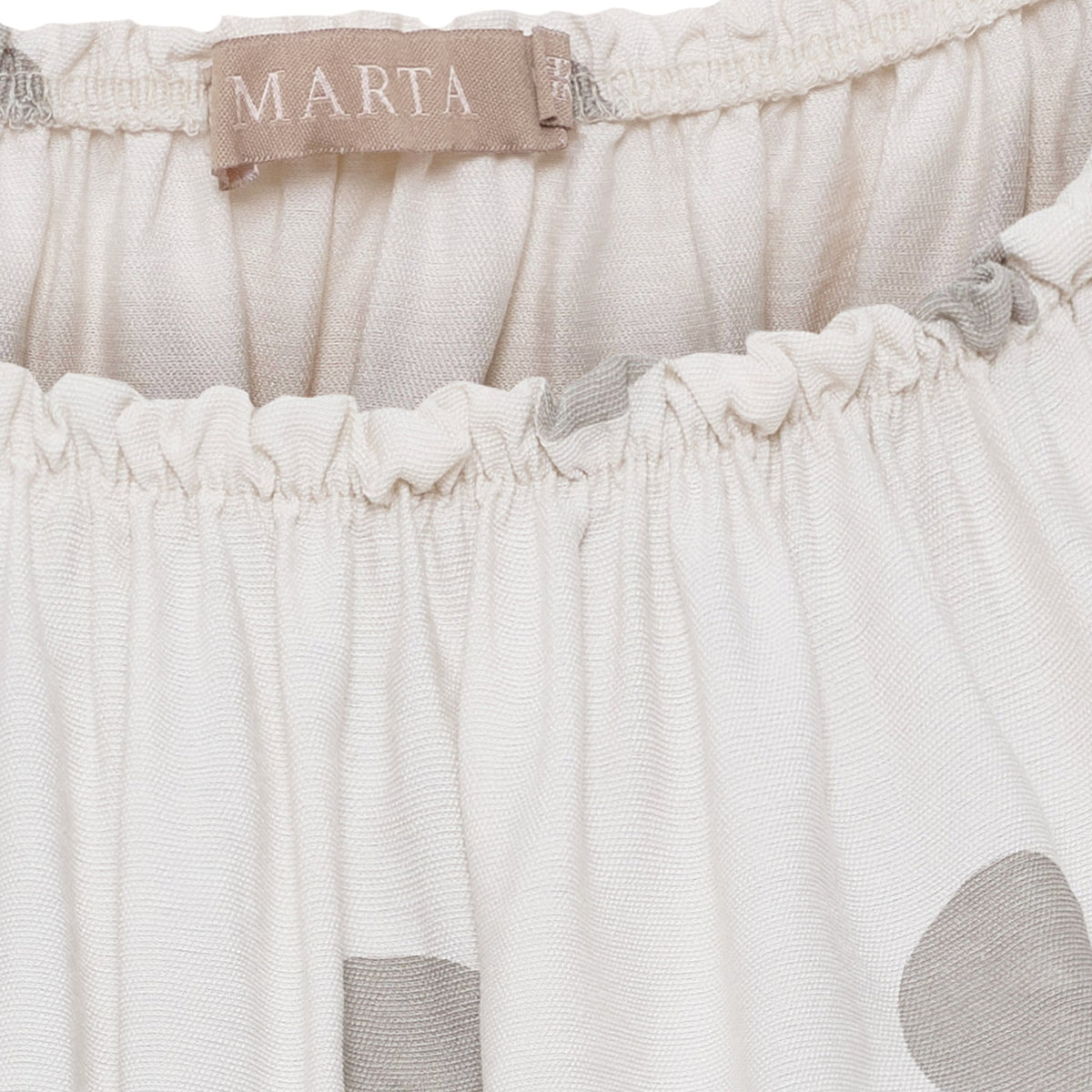 Nærbillede af Marta du Château 155063-blusens linning i beige med prikket mønster og MARTA-mærke, der giver et diskret strejf af charme.