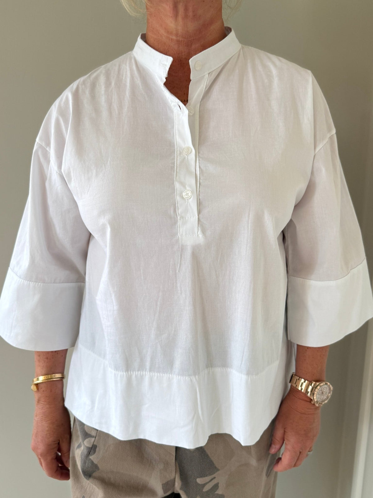 Hun har en top fra Marta du Château i farven Ginger Hvid på, beige bukser, et ur og armbånd.