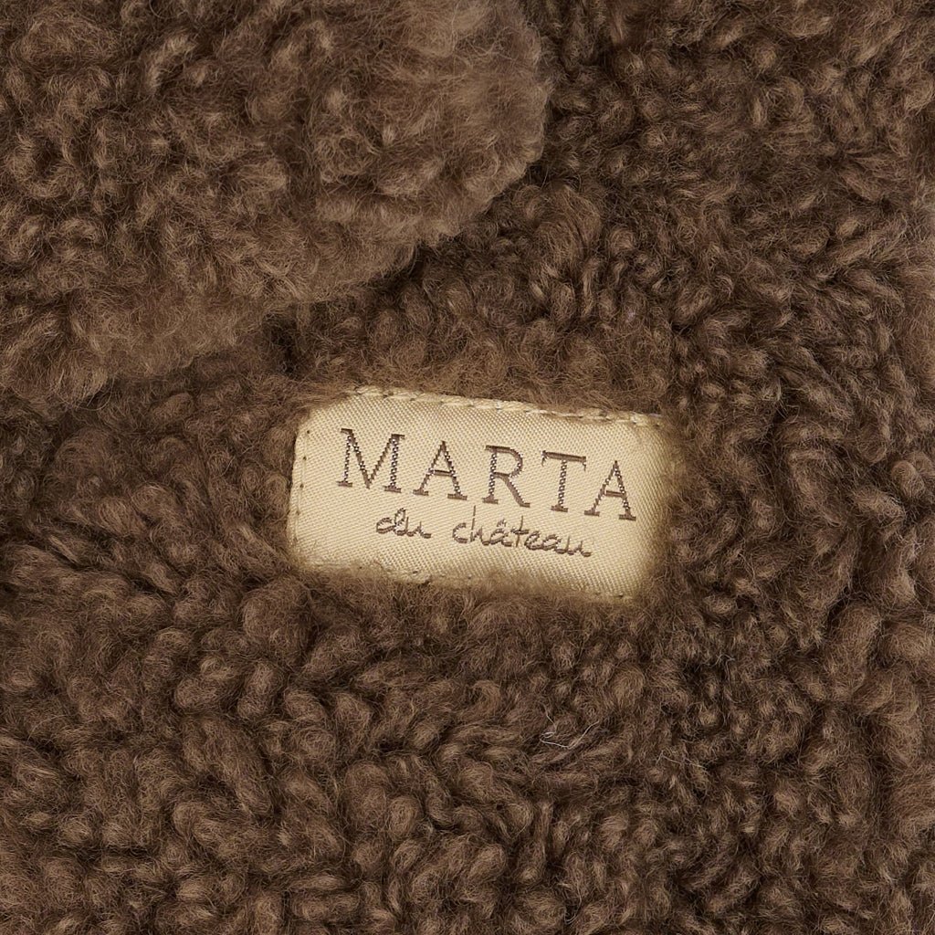 Nærbillede af MDCNadi Mørkebrun-teddy-stof fra Marta du Château med et mærke med logo syet fast på det bløde materiale.