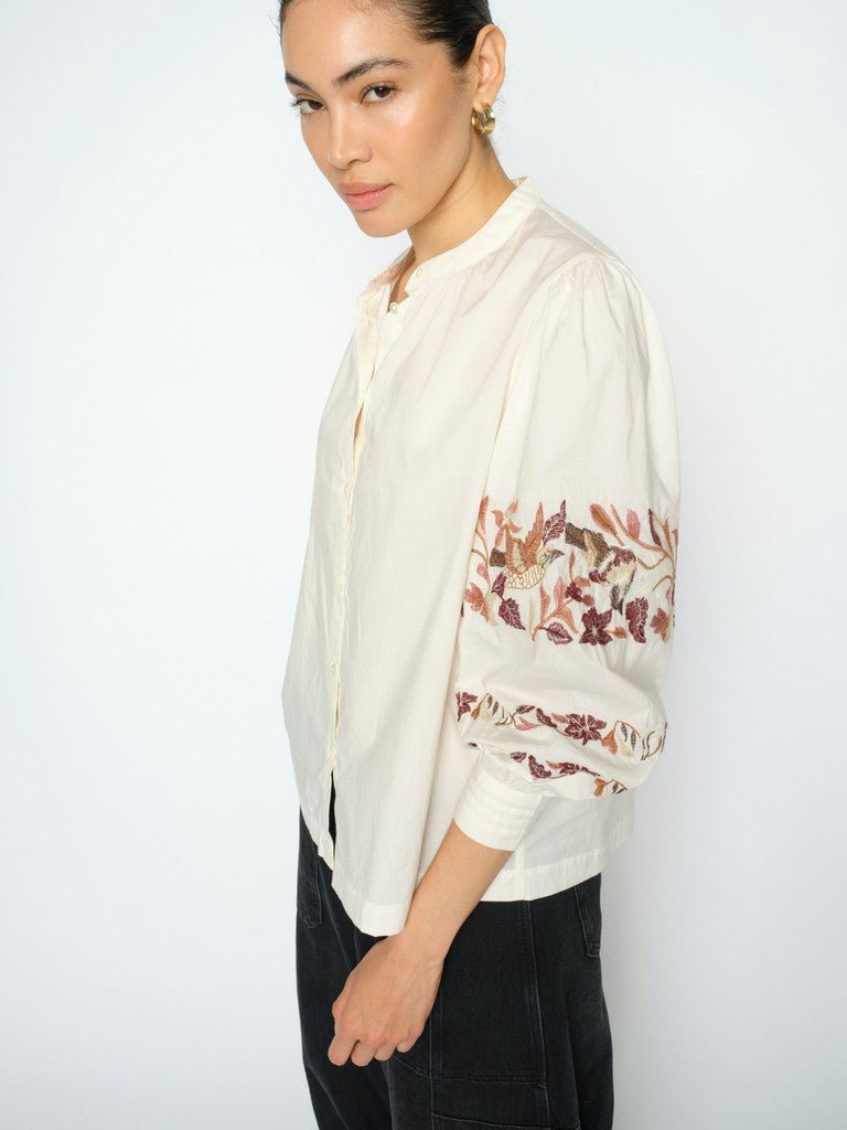 Kvinde i MOS MOSH Notto Off White-bluse, set fra siden, med blomsterbroderi på ensfarvet hvid baggrund.